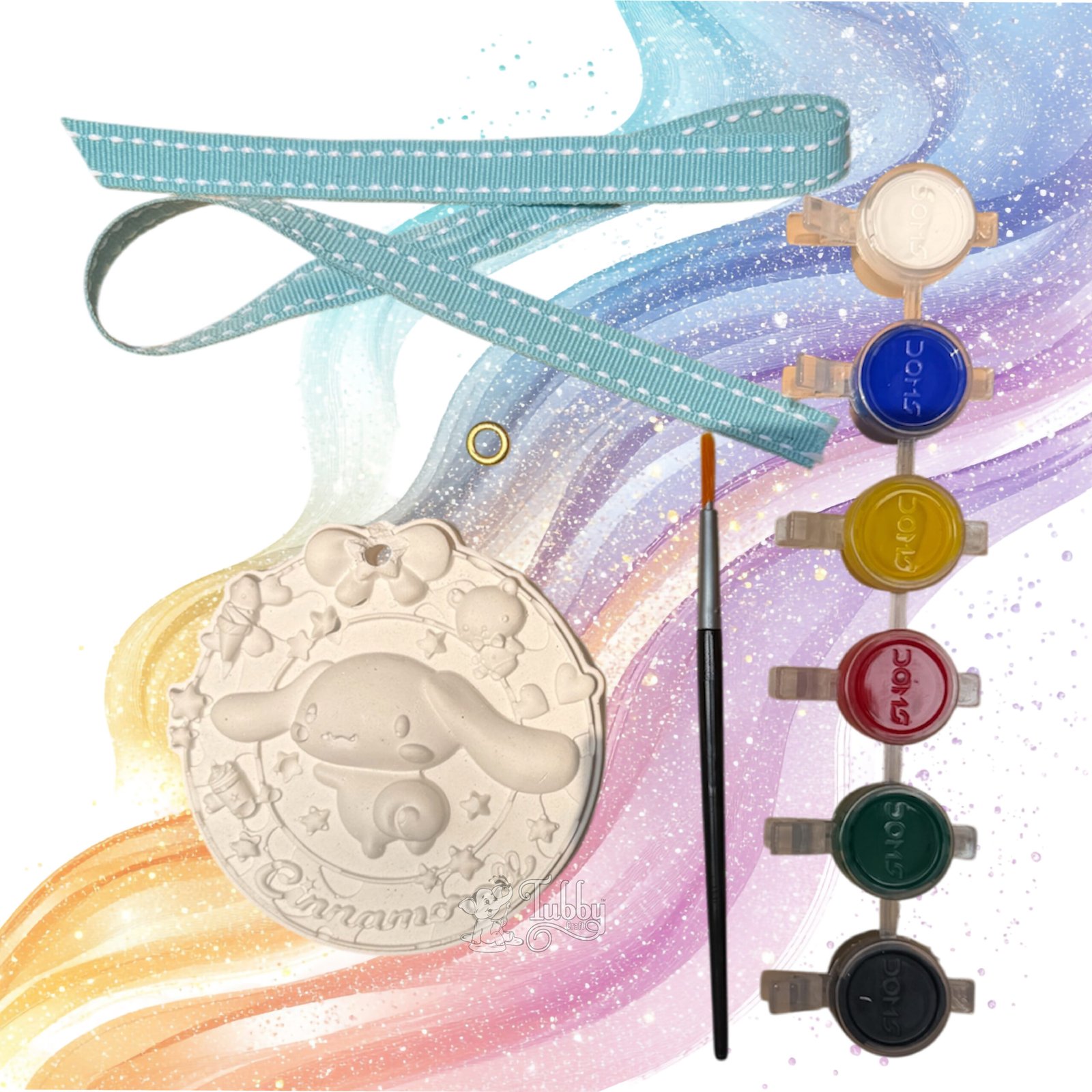 An all-in-one DIY craft kit for children displayed against a colorful, swirly pastel background. The kit features a white, 4-inch round embossed keepsake plate with a 3D design of the cartoon character Cinnamoroll floating among stars, with a partial name spelled along the bottom border. The kit also includes a fine-tip paintbrush, a strip of six vibrant acrylic paint pots, a sky blue ribbon with white contrast stitching, and a single golden metal eyelet.